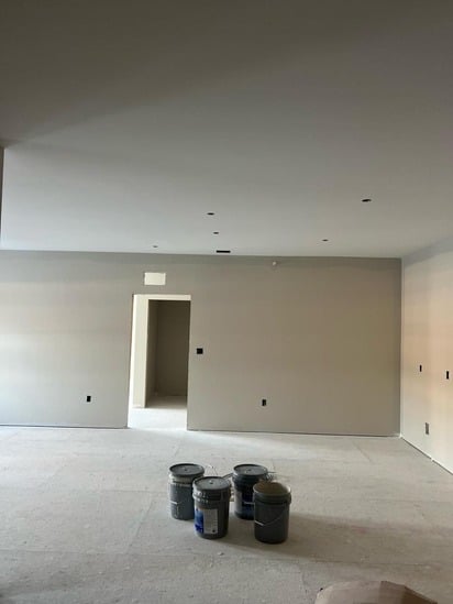 Perspective shot from a hallway entrance looking into the main space, with paint supplies highlighting the decoration phase of interior construction finishing.