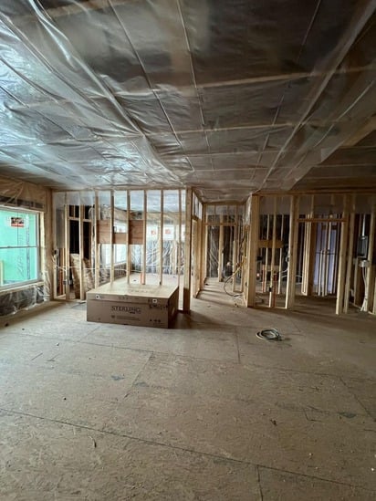 An open concept living area displaying residential interior framing with exposed wood studs, subflooring, and a ceiling vapor barrier.