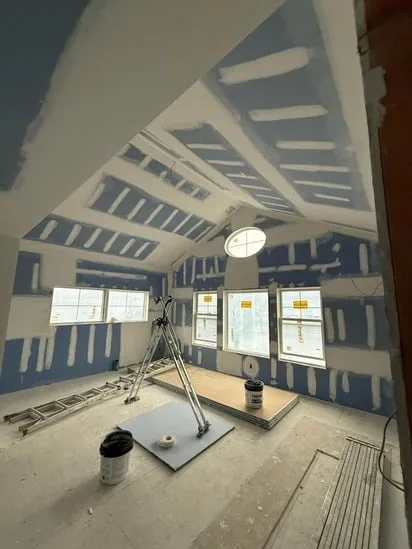 Vaulted ceiling room with a round window during the interior drywall finishing process.