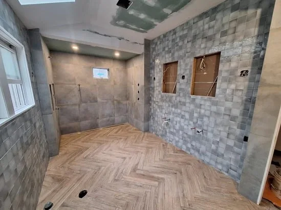 Broad angle of the bathroom tile installation showing the structural progress and contrasting tile selections.